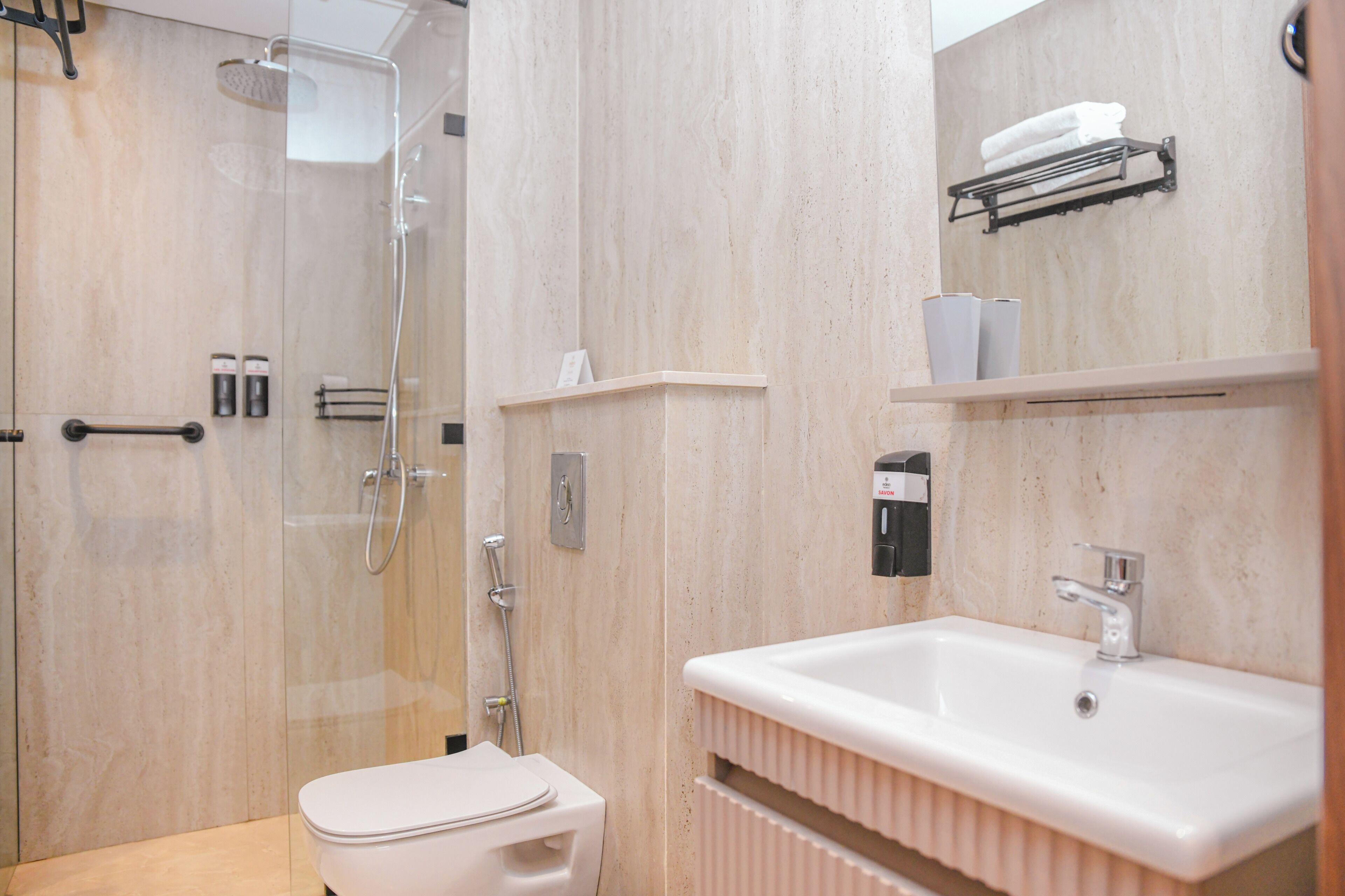 Une salle de bain moderne avec une douche à parois de verre, des toilettes blanches, un lavabo avec un miroir et un porte-serviettes.
