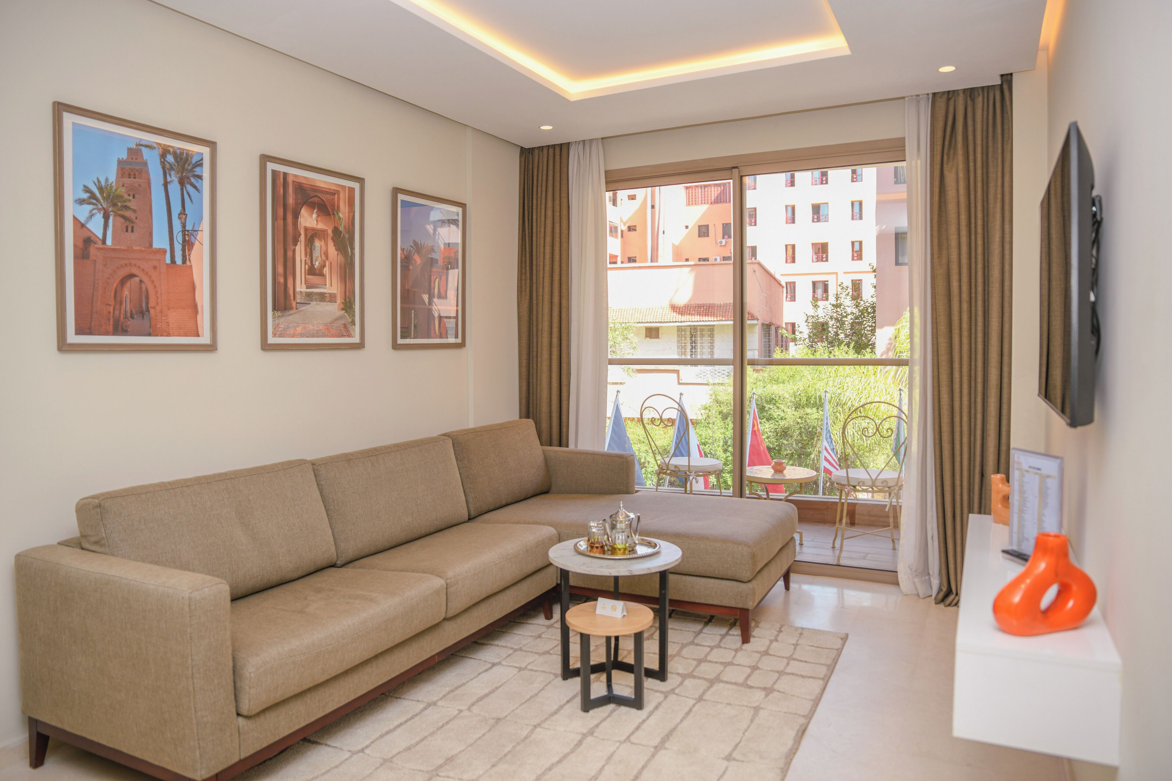 Ein Wohnzimmer mit einer Couch, einem kleinen runden Tisch mit Tablett und einem Balkon mit Blick auf Gebäude und Flaggen.