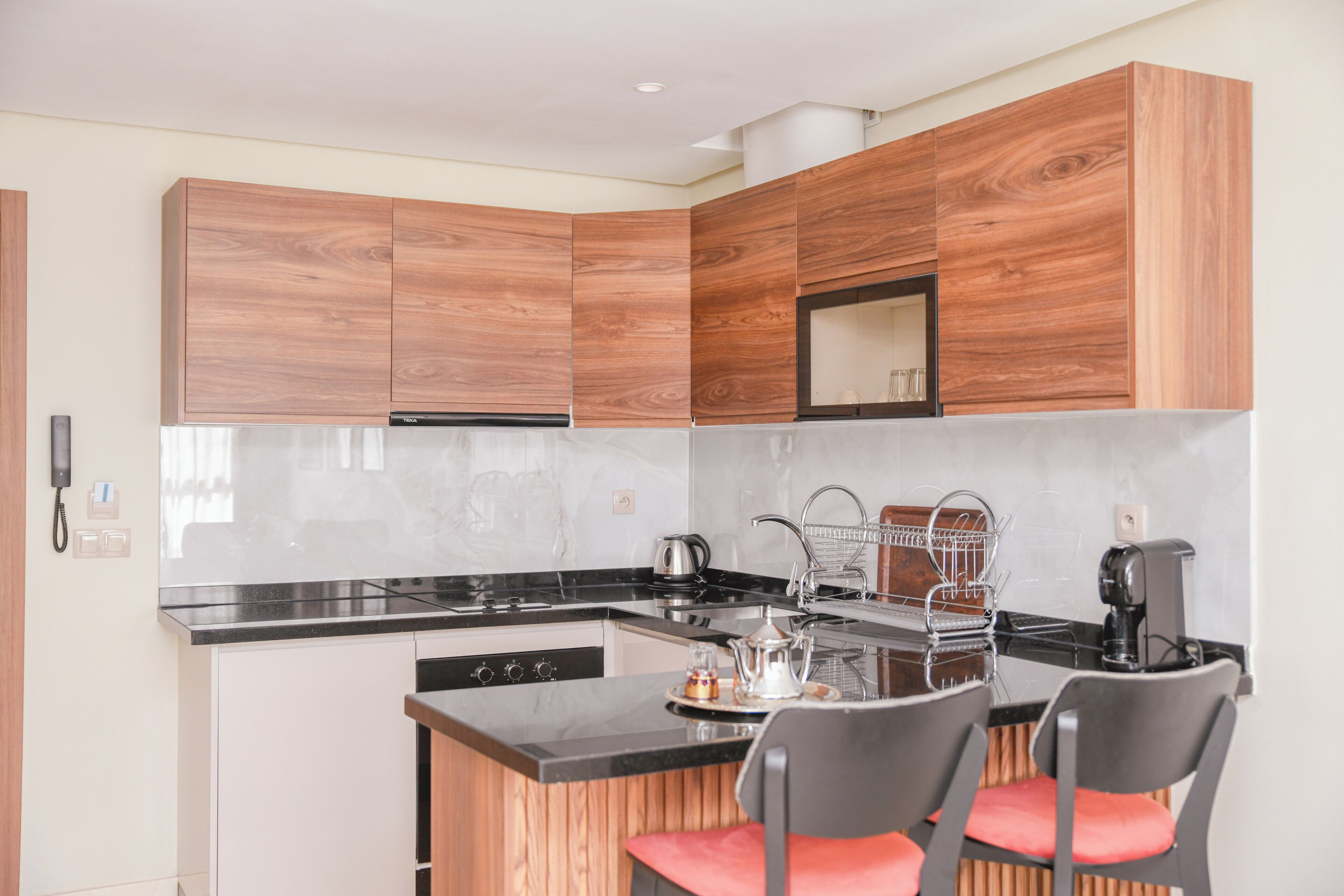 A modern kitchen with wooden cabinets, a black countertop, a stove, a sink, and two bar stools.