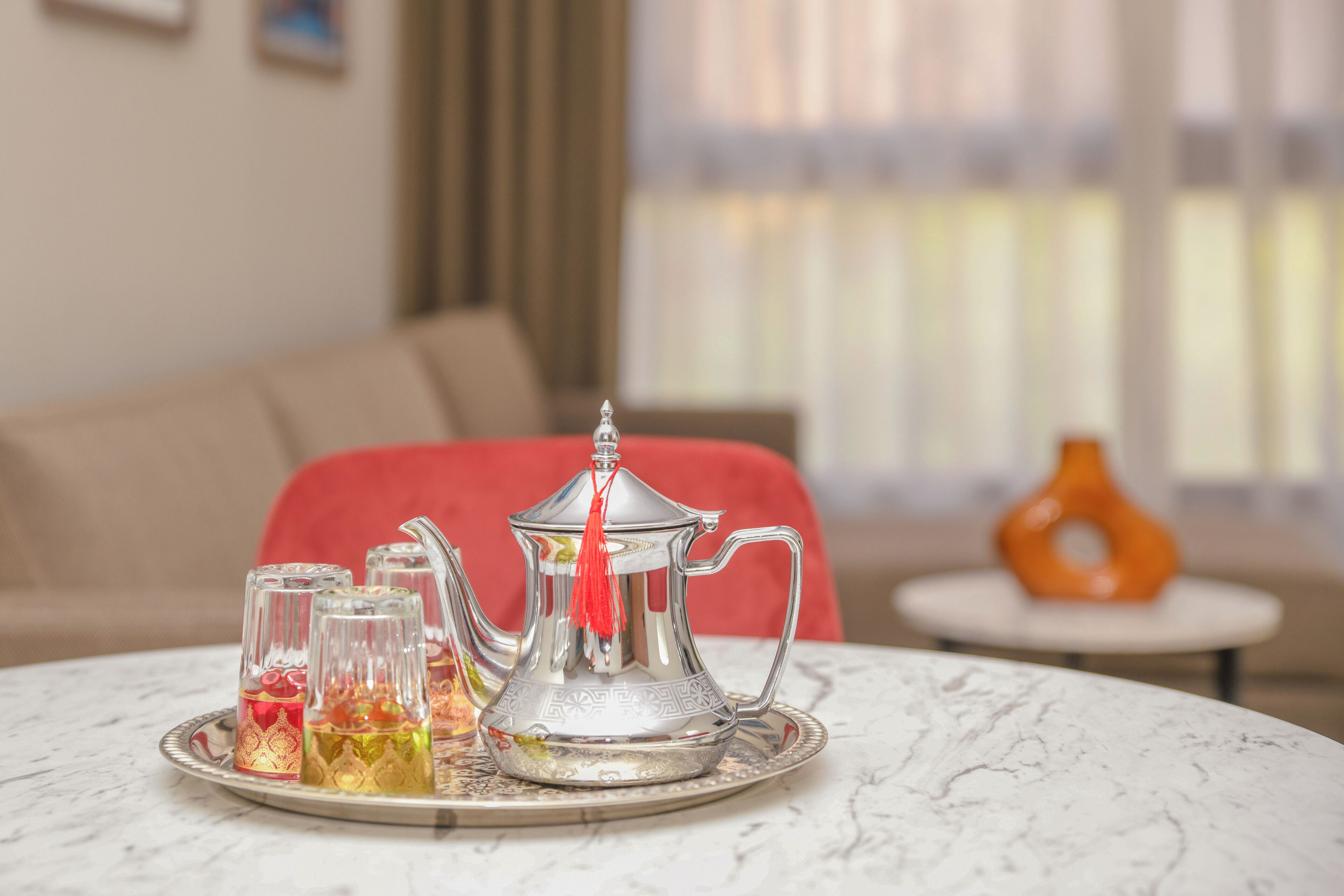 Une table avec une théière en argent, des verres et un plateau, dans une pièce où se trouvent un canapé et un vase.