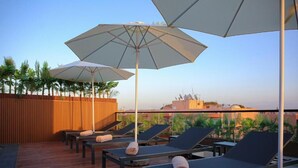 A rooftop lounge area with sun loungers, umbrellas, and a wooden deck. - Résidence Eden Marrakech (Marrakech)