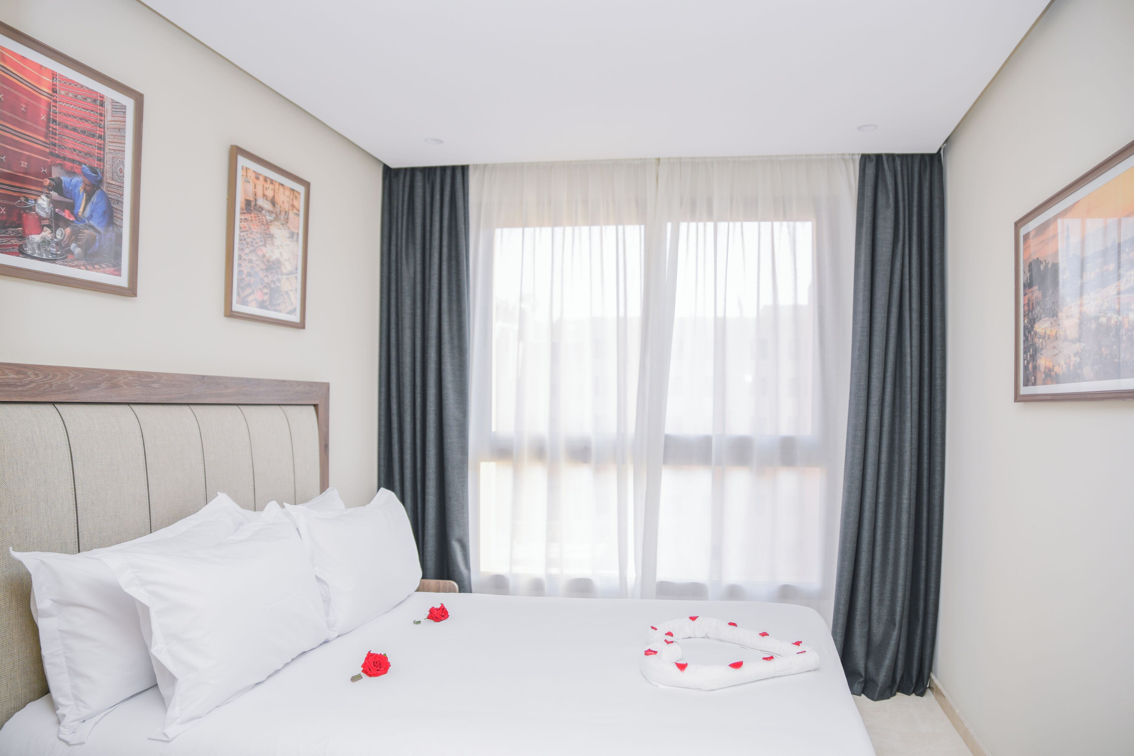 A hotel room with a bed, curtains, and two framed pictures on the wall.
