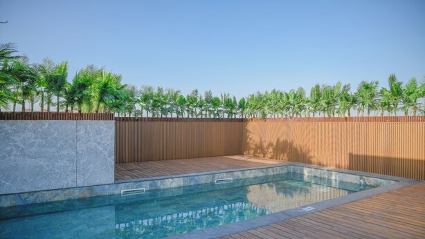 A swimming pool with a wooden deck and a stone wall, surrounded by a wooden fence and palm trees. - Résidence Eden Marrakech (Marrakech)