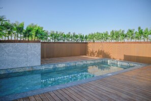 Ein Swimmingpool mit Holzdeck und Steinmauer, umgeben von einem Holzzaun und Palmen.