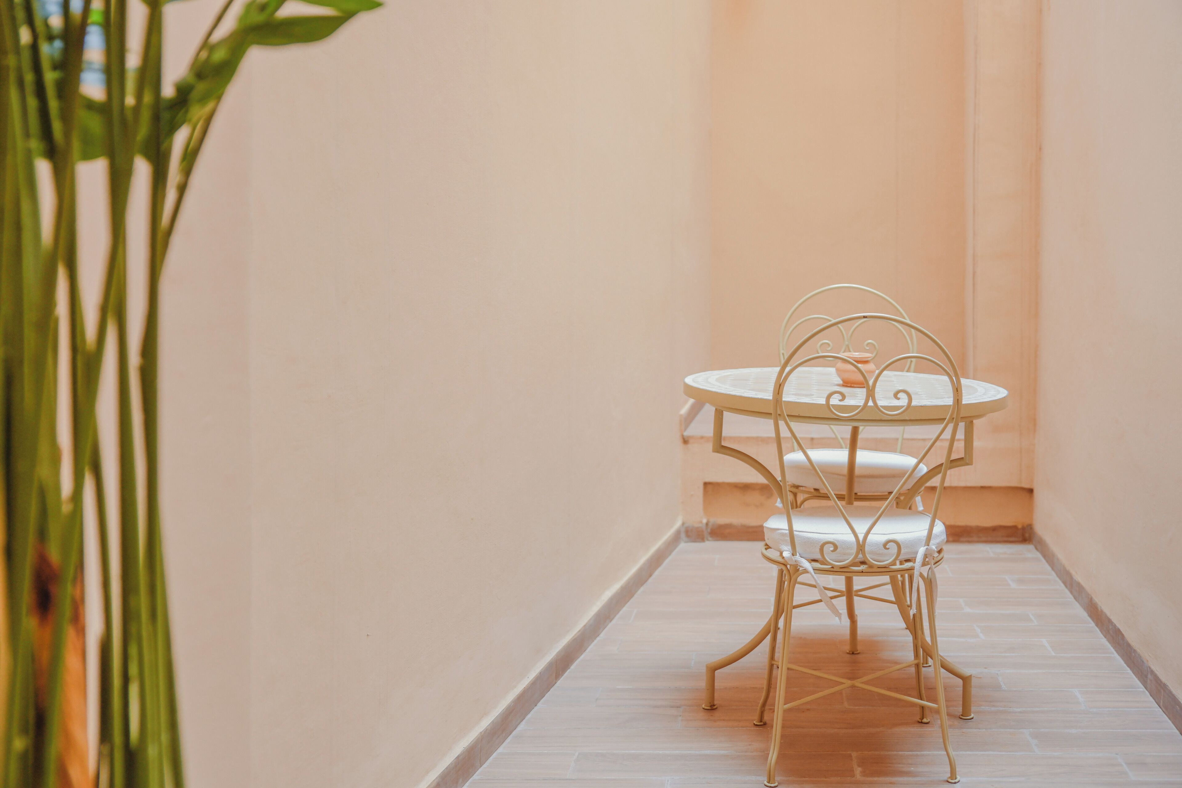 A narrow corridor with a white metal table and chairs, a potted plant, and a tiled floor.