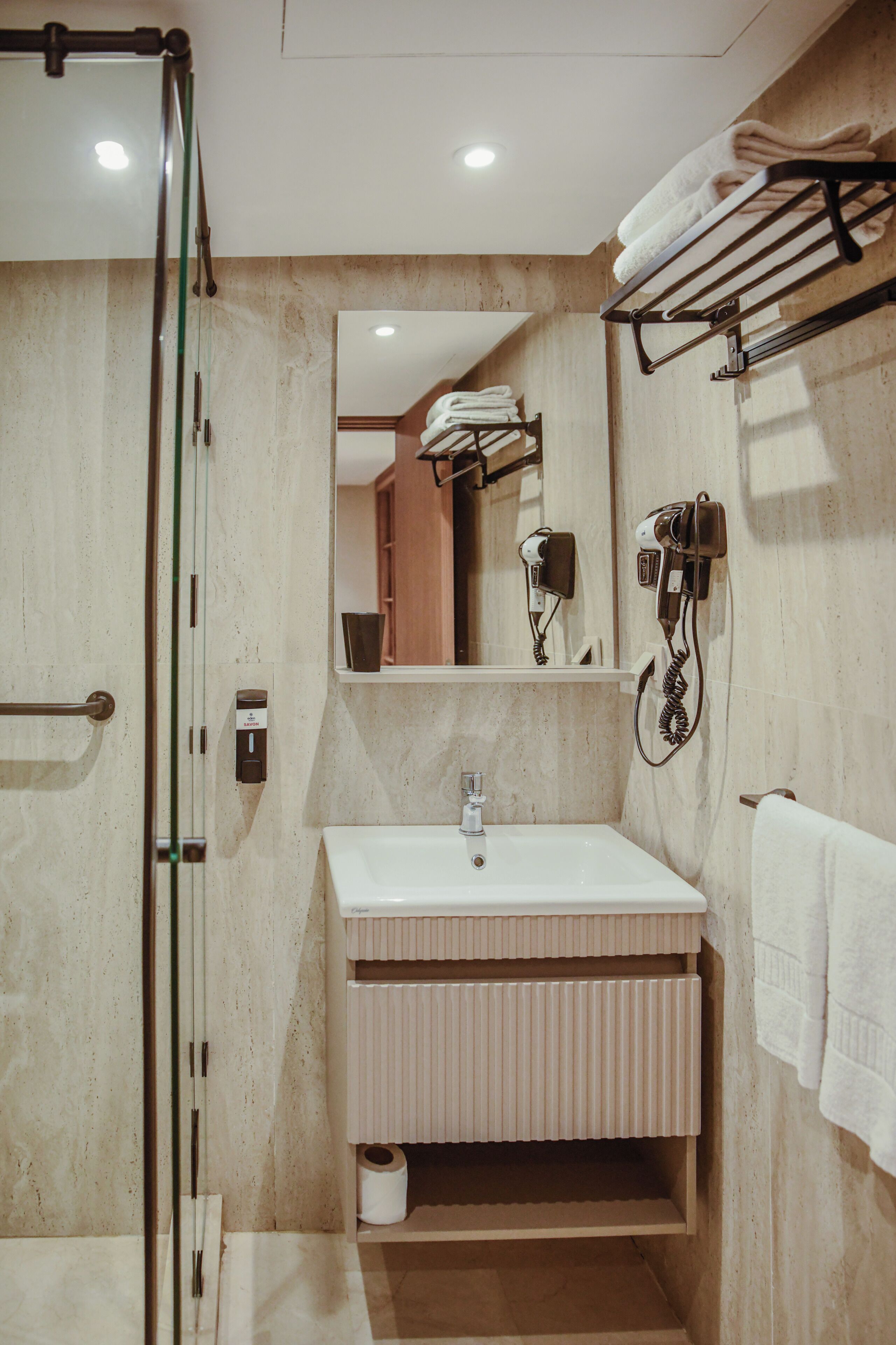 A modern bathroom with a glass shower enclosure, a white sink, and a towel rack.