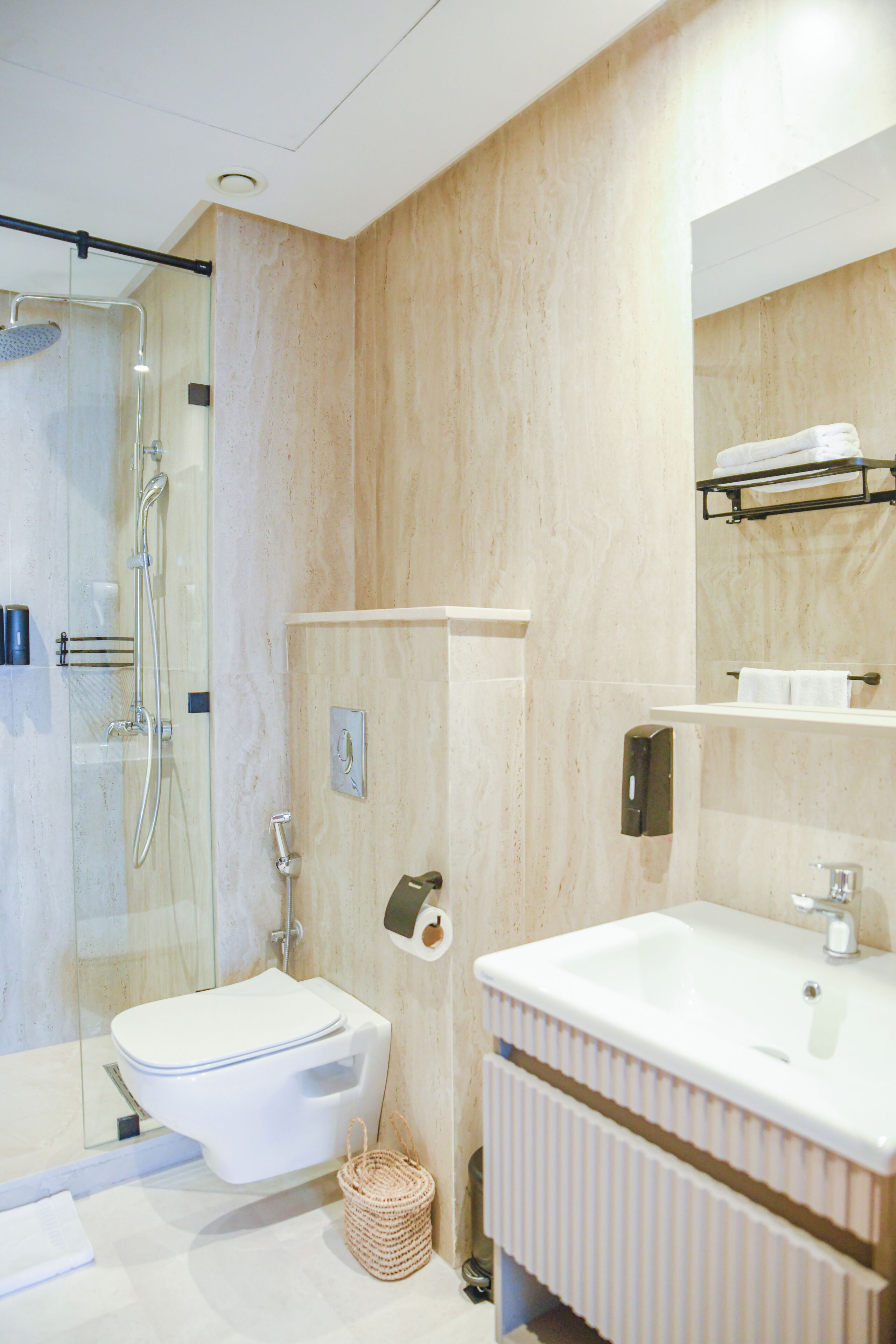 Un baño moderno con cabina de ducha de vidrio, inodoro blanco, lavabo con espejo y toallero.