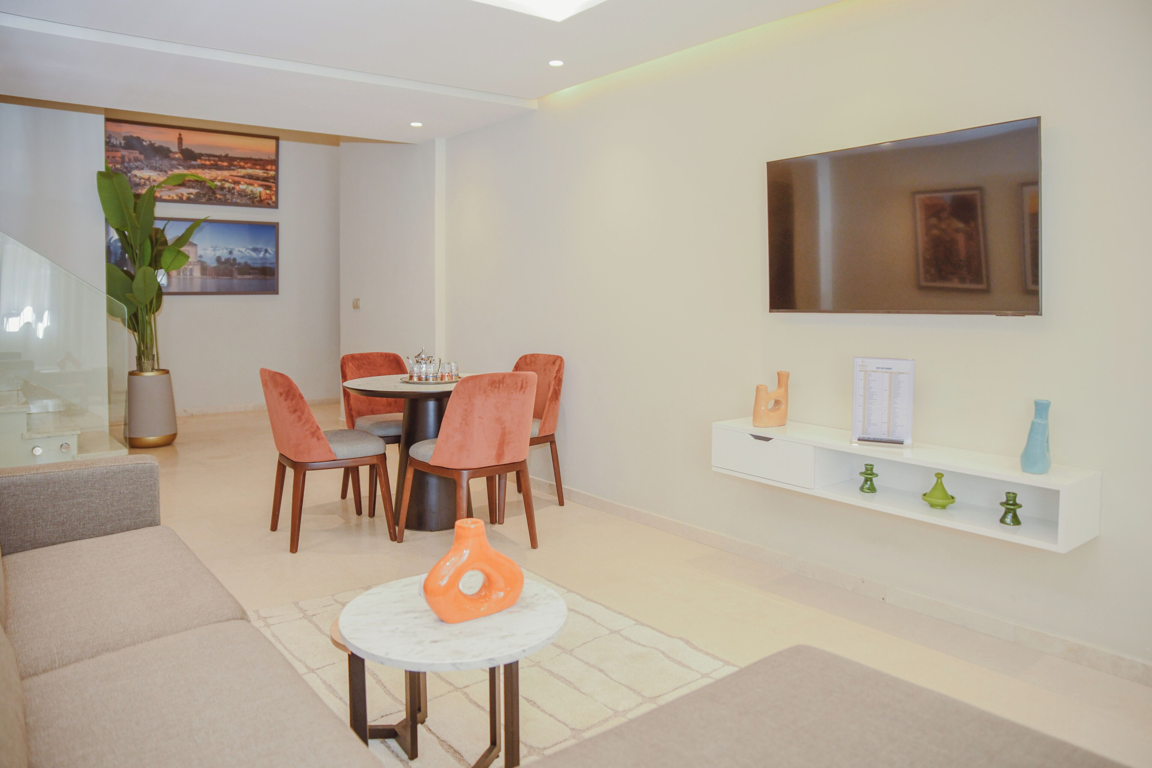 Un salon moderne avec un coin repas, un téléviseur fixé au mur et une plante.