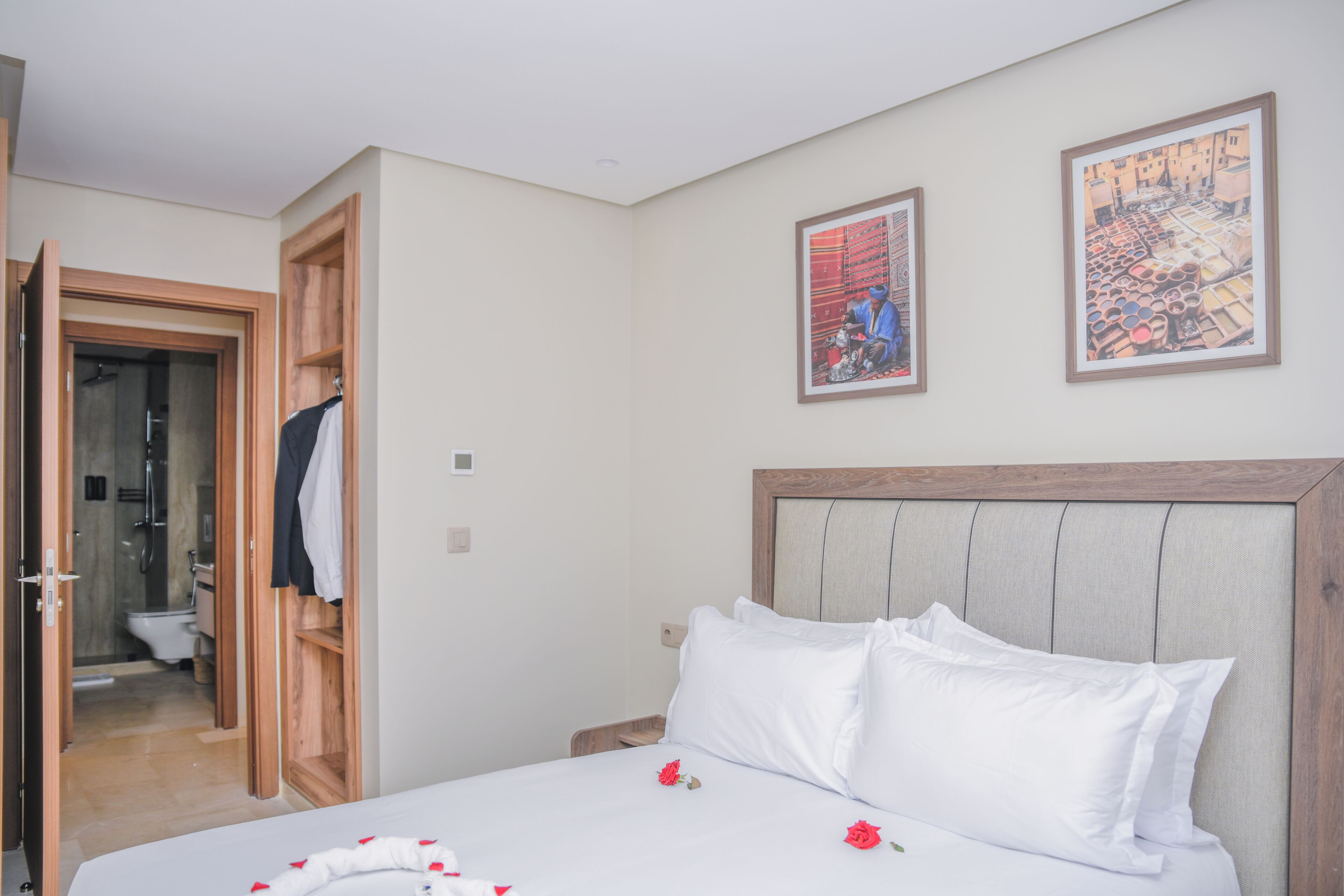 A hotel room with a bed, a wooden headboard, a wardrobe, and a bathroom visible through an open door.