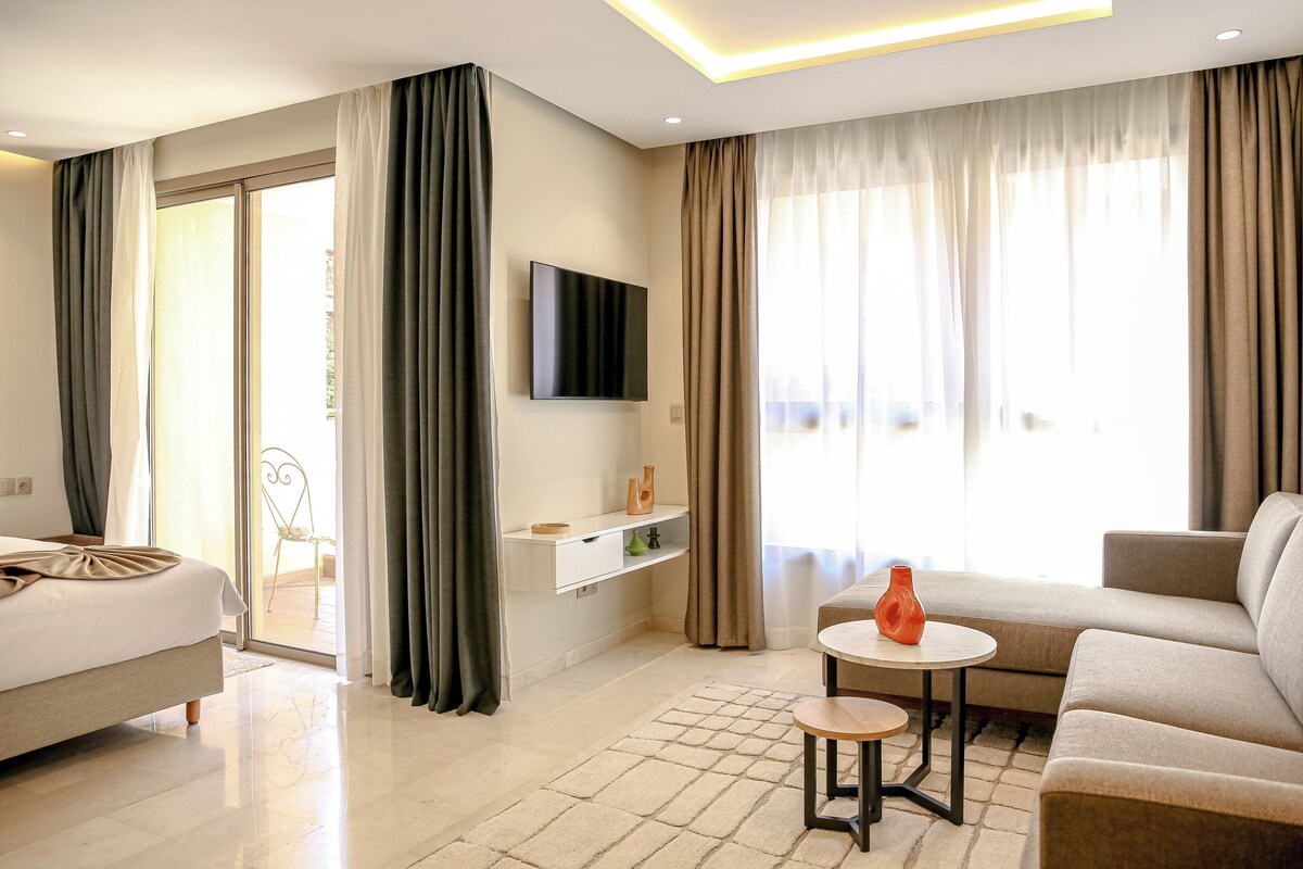 A modern hotel room with a bed, a sofa, a TV, and a small table.