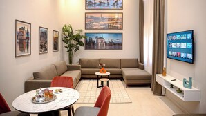 A modern living room with a sectional sofa, a dining table with a tray of snacks, a TV mounted on the wall, and framed cityscape pictures. - Résidence Eden Marrakech (Marrakech)