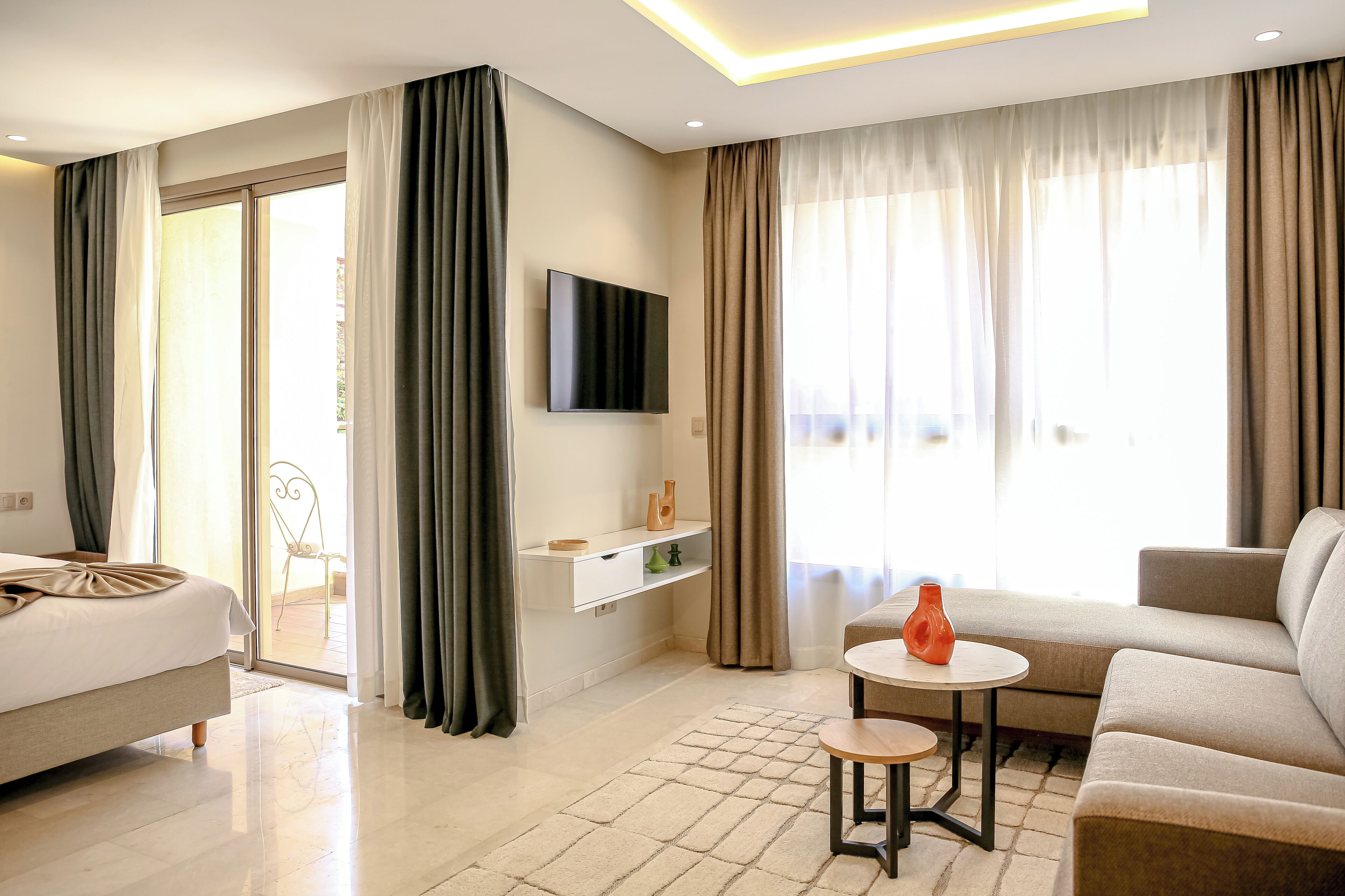Quarto de hotel moderno com cama, sofá, televisão e uma pequena mesa.
