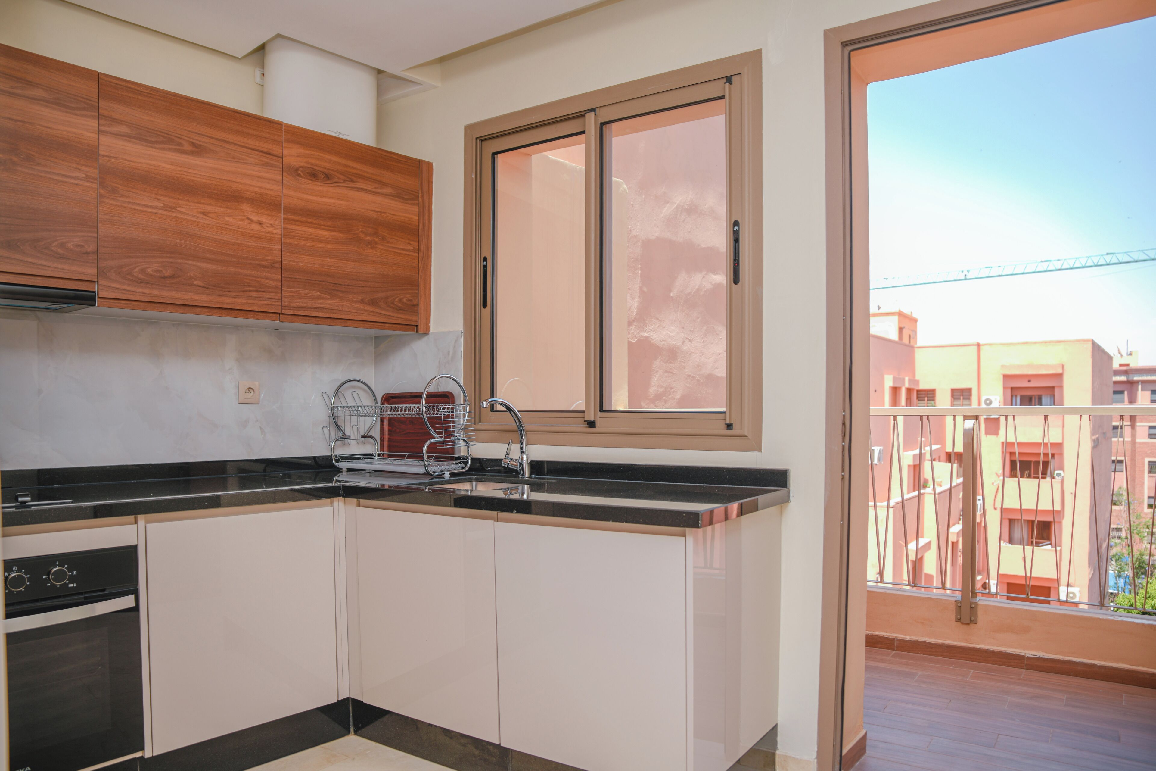 Uma cozinha moderna com armários brancos, bancada preta e janela com vista para edifícios.