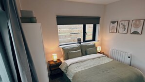 Quarto com cama, luminárias de cabeceira, janela e radiador.