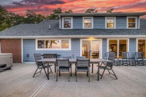A two-story house with a patio area featuring a dining table and chairs, a brick wall, and a covered outdoor seating area. - Escape to Hilltop Estate—a newly renovated 5BR, 3BA mountain retreat (Blue Ridge)