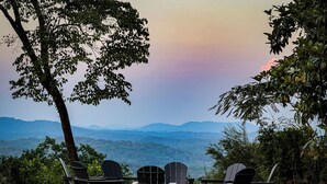 Vista de una zona verde con sillas Adirondack y una mesa, con vistas a un paisaje montañoso.