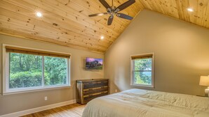 Un dormitorio con techo inclinado, ventanas amplias, un aparador de madera y una cama.