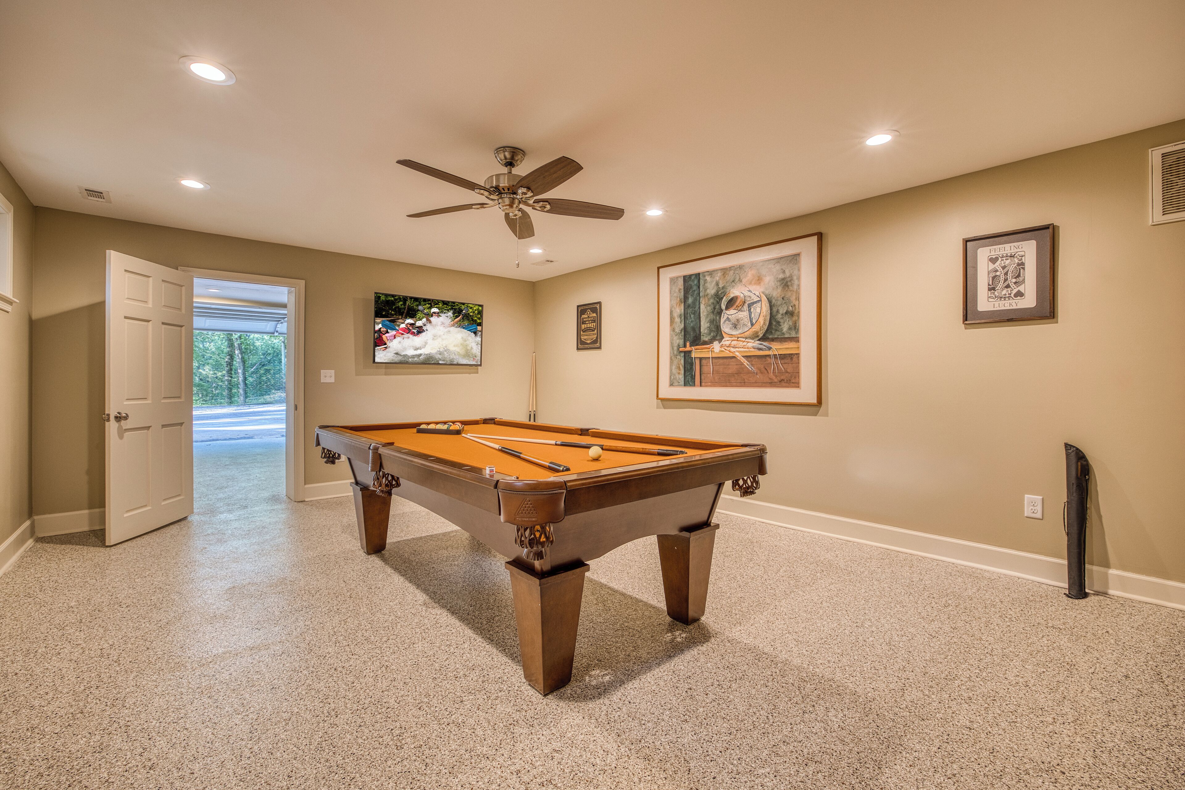 A pool table in a room with beige walls, a ceiling fan, and framed artwork.