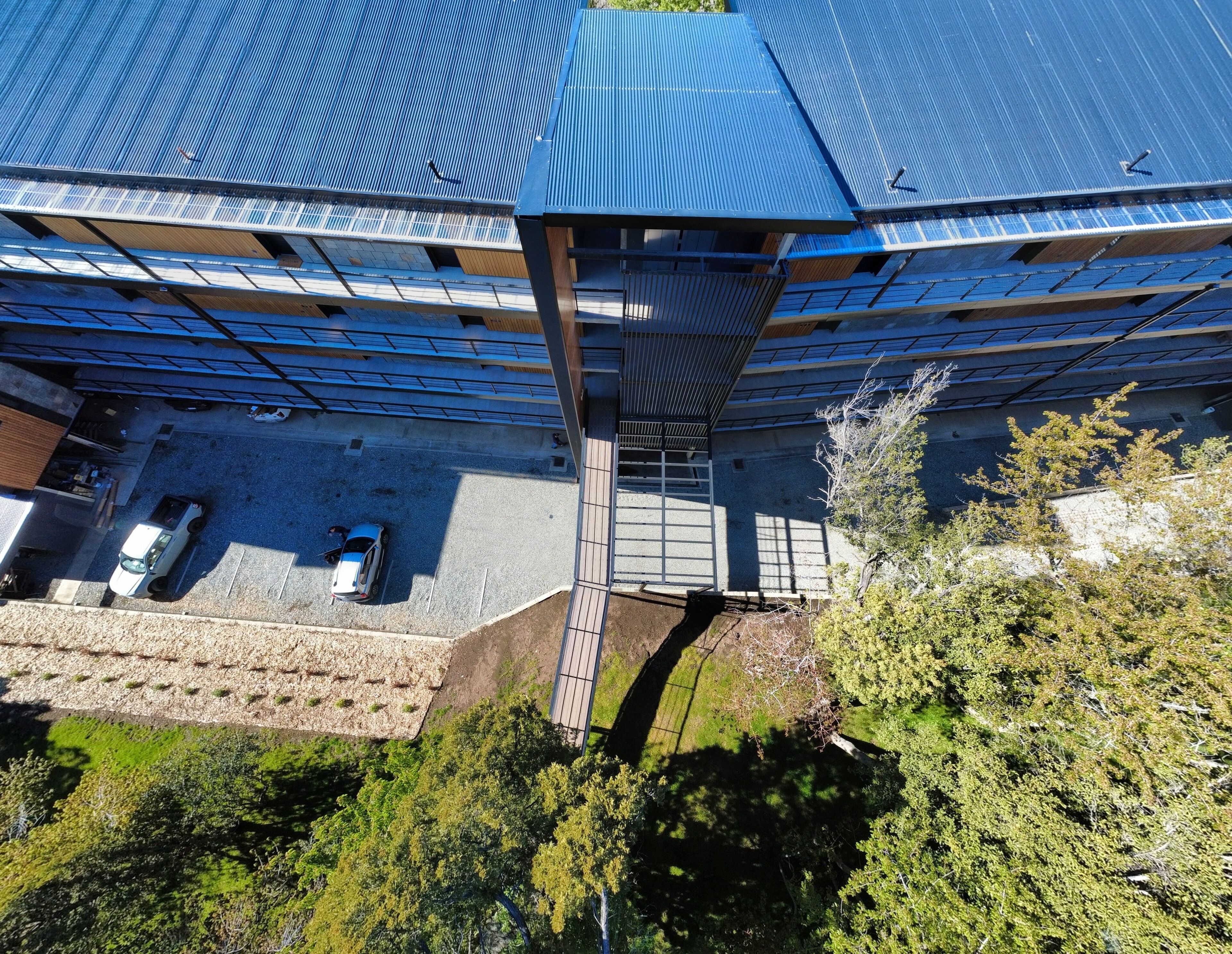 Luchtbeeld van een gebouw met een blauw dak, zonnepanelen en een parkeerplaats met twee auto's.