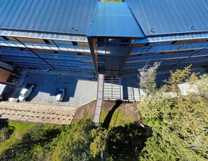 An aerial view of a building with a blue roof, solar panels, and a parking area with two cars. - Calido departamento con vista al Nahuel Huapi en Bariloche (San Carlos de Bariloche)