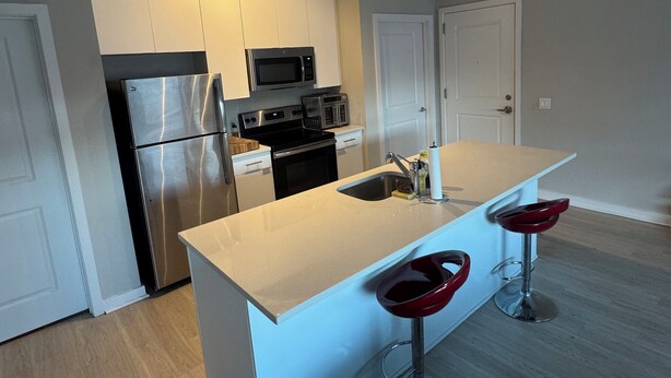 A modern kitchen with stainless steel appliances, a central island with stools, and white cabinetry. - Modern 2BR/2BTH near DC; Walk to Mall, Shops & Metro! (Hyattsville)