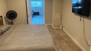 A bedroom with a bed, a standing fan, a television, and a door leading to a balcony. - Modern 2BR/2BTH near DC; Walk to Mall, Shops & Metro! (Hyattsville)