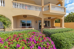 A two-story building with balconies, a covered patio, and a well-maintained garden with colorful flowers. - The Strand apartment 1A, 5 guests with pool and beach (Willemstad)
