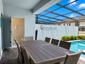 Un patio exterior con piscina, una mesa con sillas y un área cubierta con vista al cielo.