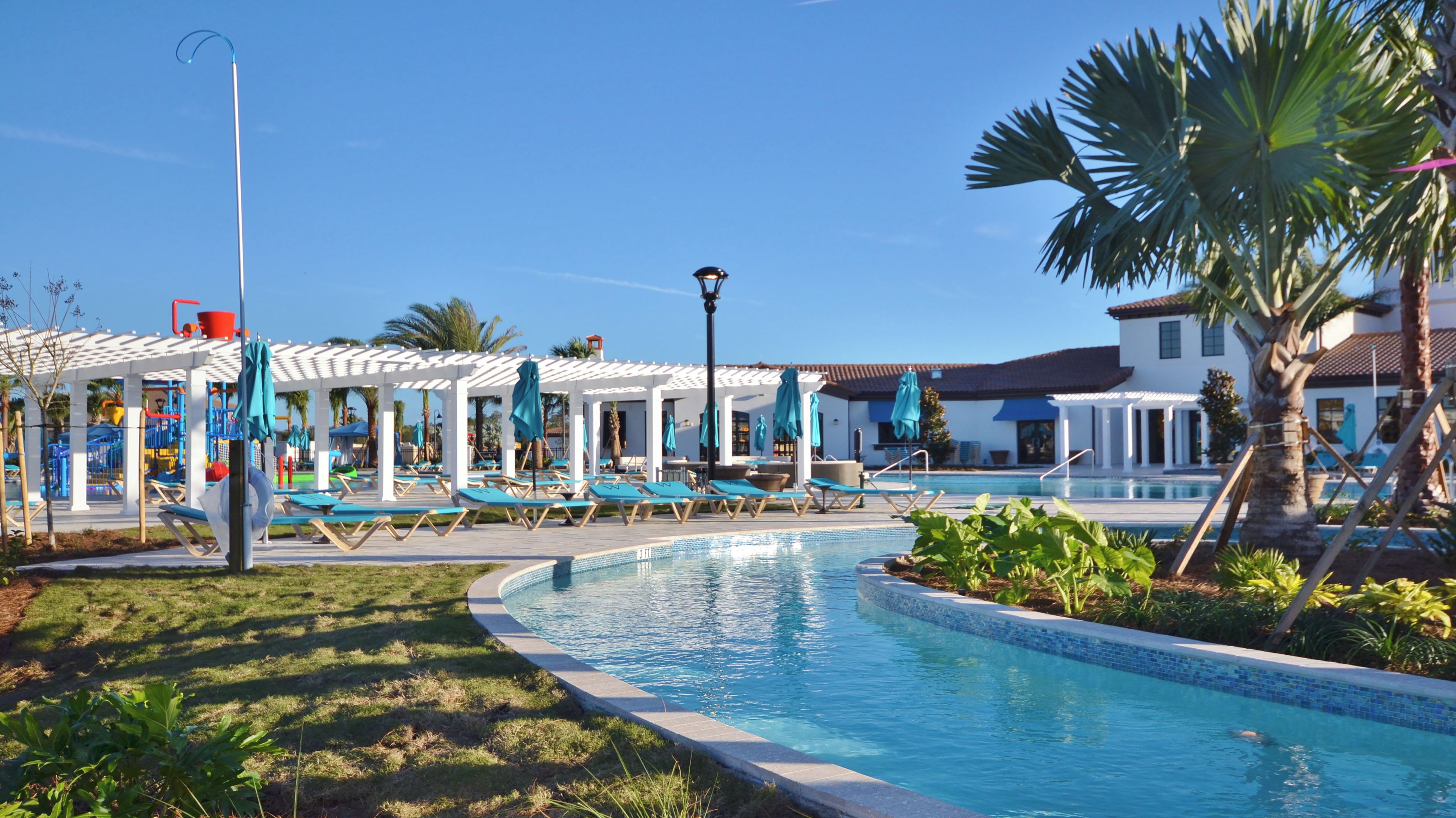 A pool area with lounge chairs and umbrellas, a covered seating area, and a building with a tiled roof.