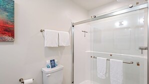 Ein modernes Badezimmer mit Duschkabine aus Glas, Toilette und zwei Handtüchern, die an der Wand hängen.