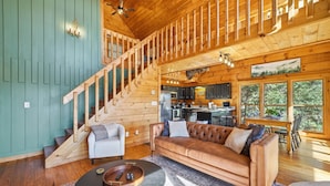 A wooden cabin interior with a staircase, a sofa, a dining table, and a kitchen area. - Best views in Cherry Log, Putting Green, Hot Tub (Cherry Log)