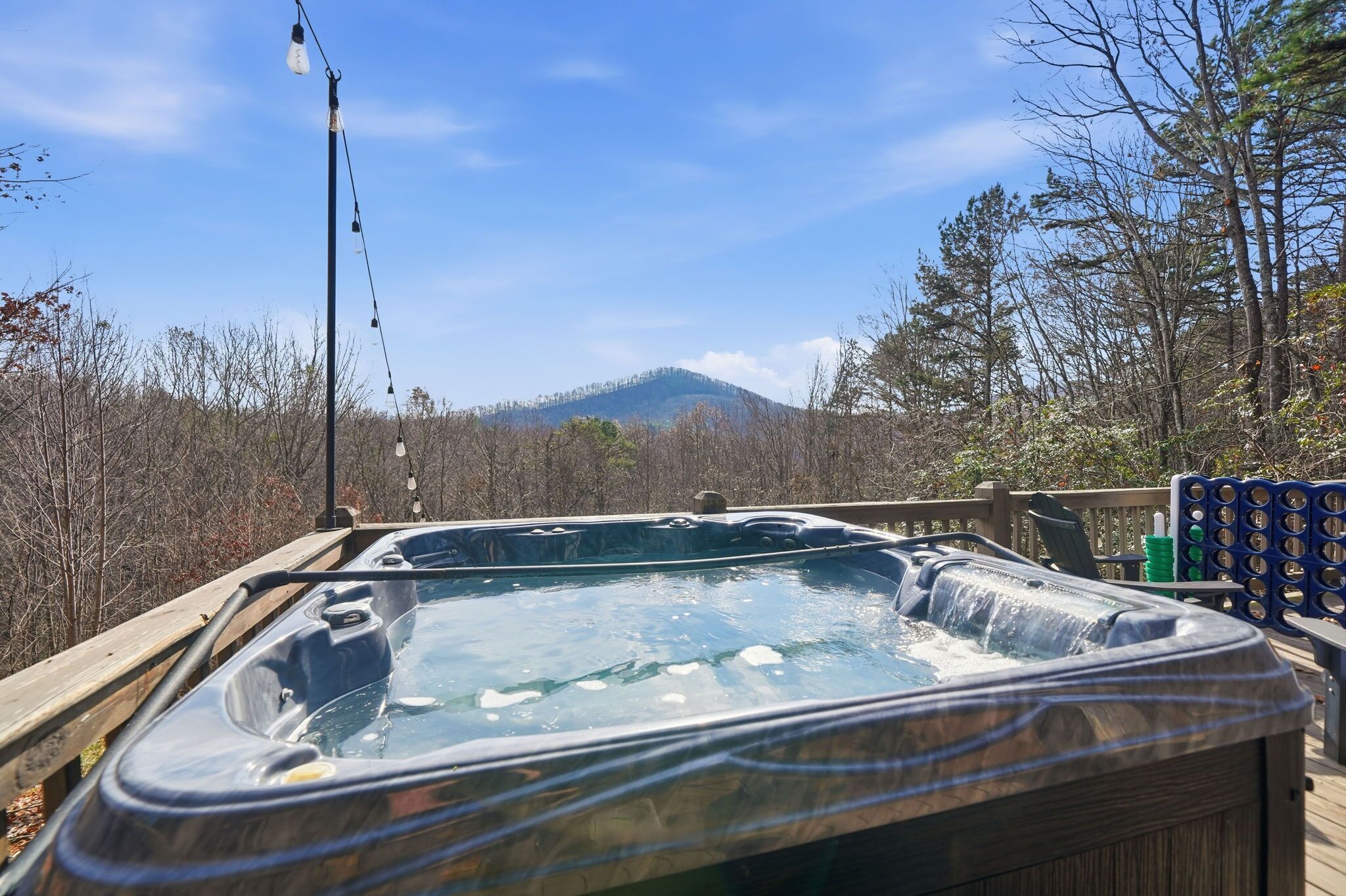 A hot tub on a wooden deck with a view of a mountain and forest.