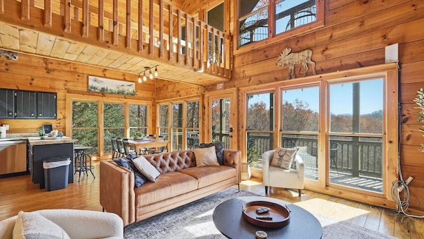 A spacious cabin interior with a loft bedroom, a cozy living area with a leather sofa, and large windows offering views of the surrounding forest. - Best views in Cherry Log, Putting Green, Hot Tub (Cherry Log)