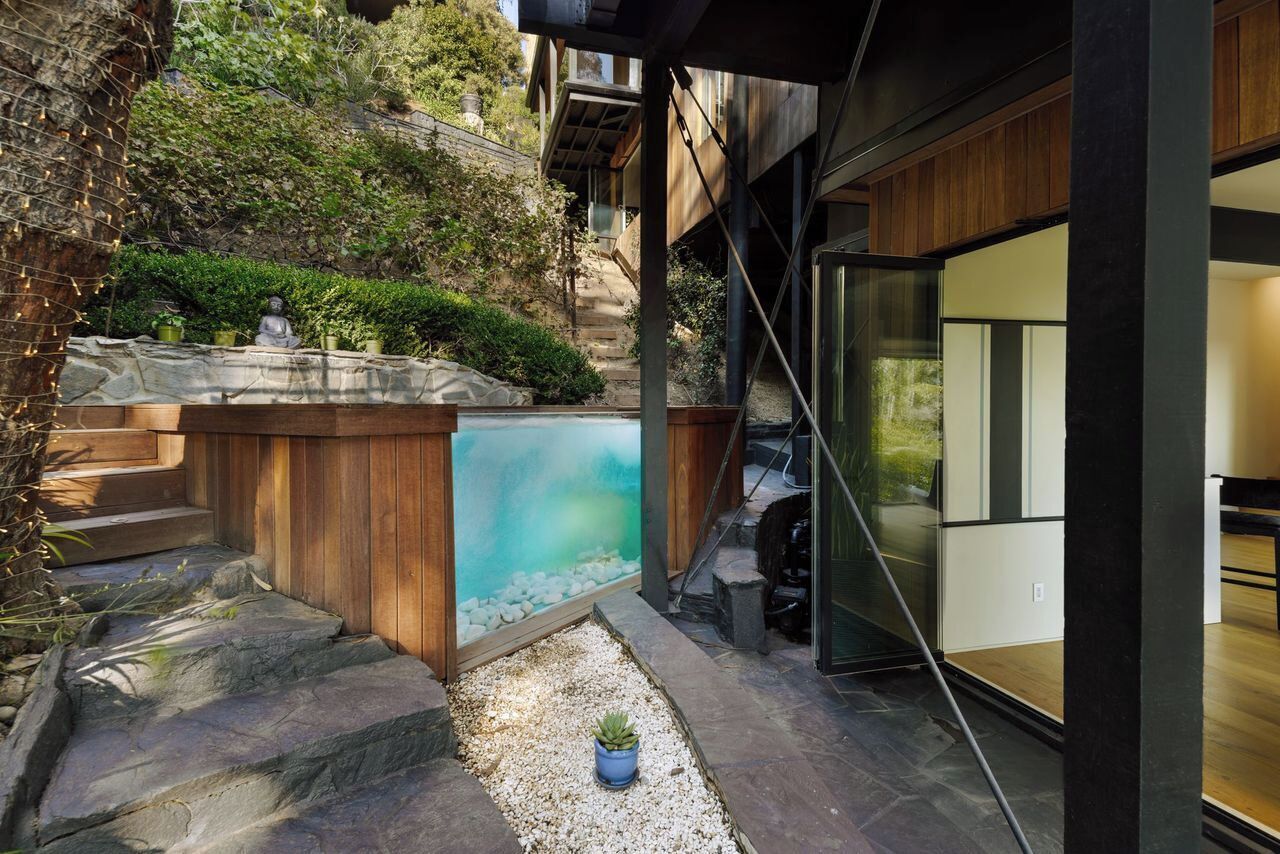 A modern outdoor area with a stone staircase leading to a wooden deck, a small pool, and a seating area with a statue.