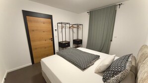 Un dormitorio con cama, puerta de madera, armario, perchero y ventana con cortinas.