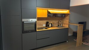 Una cocina moderna con armarios oscuros, horno empotrado, lavamanos y encimera de madera.