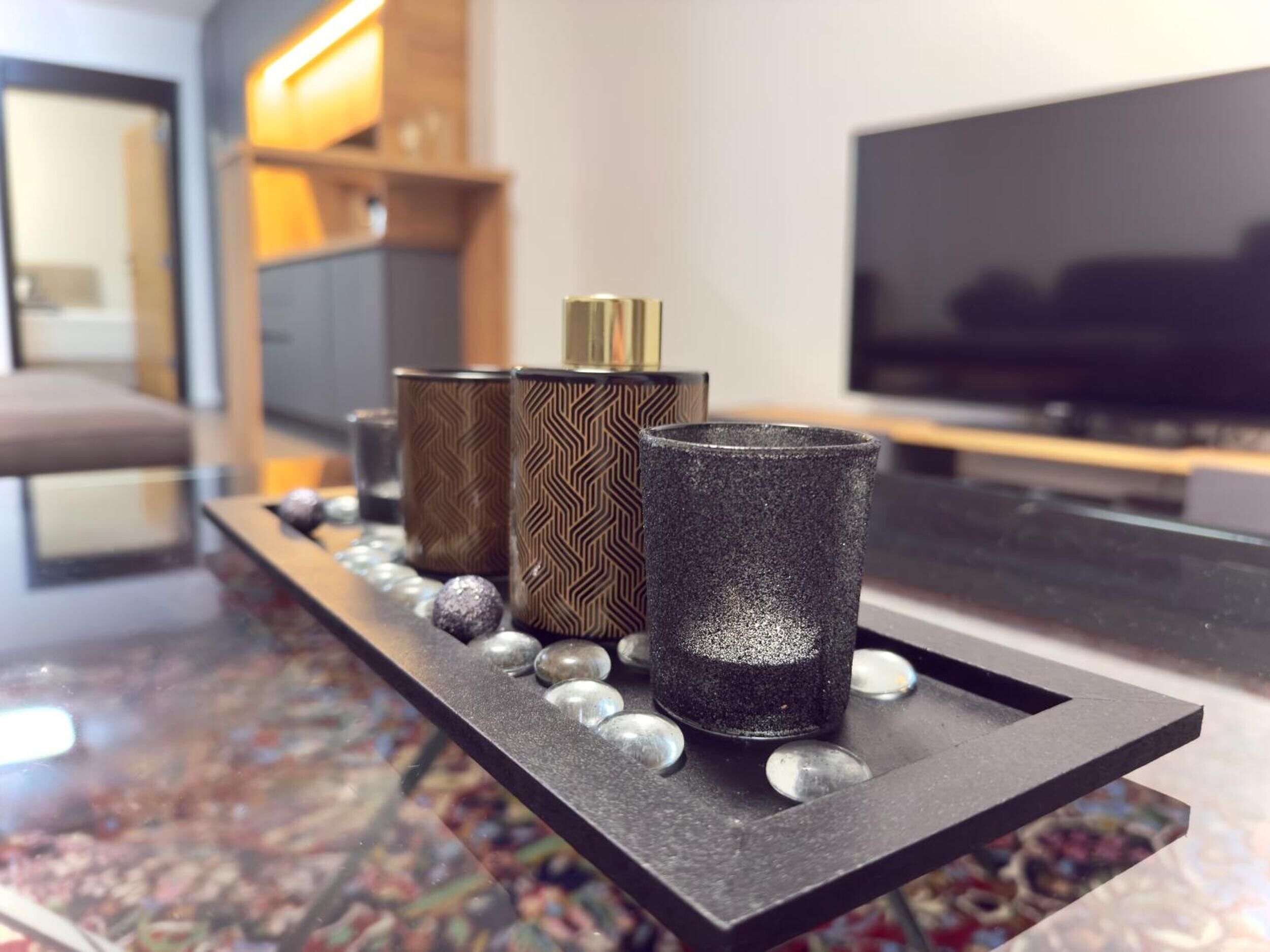Een moderne woonkamer met een zwarte dienblad waarop decoratieve spullen staan, een televisie en een houten kast op de achtergrond.