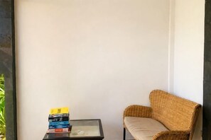 A corner with a wicker chair, a small table with a stack of books, and a plain wall. - The Confidential Mandalika (Lombok)