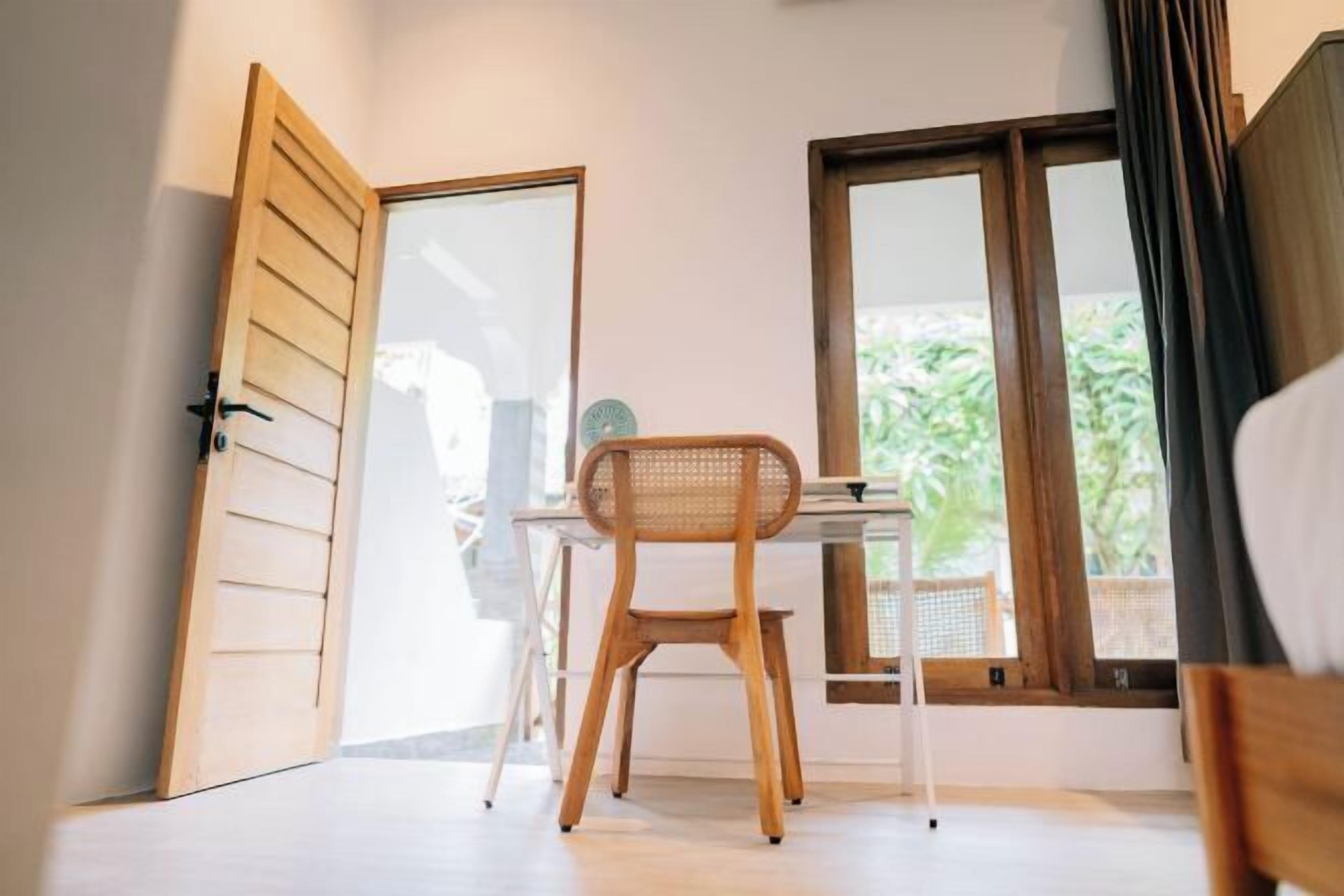 Une pièce avec un bureau en bois, une chaise et une fenêtre donnant sur un paysage verdoyant.