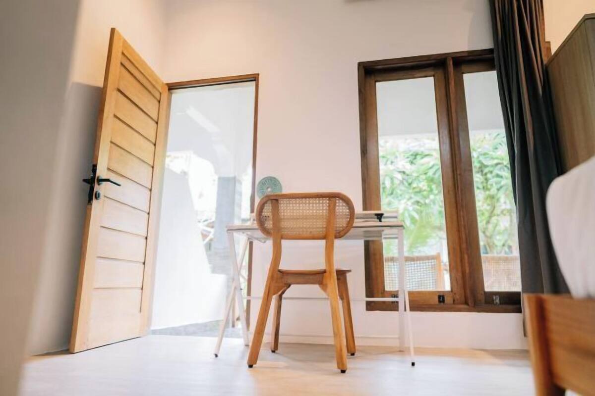 A room with a wooden desk, a chair, and a window with a view of greenery.