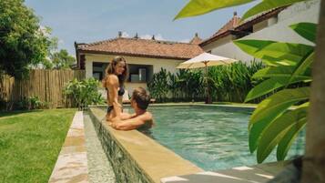 A swimming pool with a tiled edge, surrounded by a wooden fence and greenery.