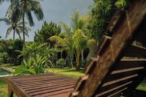 A wooden bench in a lush garden with palm trees and a pool. - The Confidential Mandalika (Lombok)