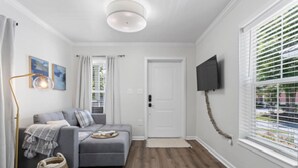 En moderne stue med en grå sofa, en gulvlampe og et fladskærms-tv monteret på væggen.
