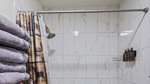 Une salle de bain avec une douche, des murs carrelés, un porte-serviettes avec des serviettes et un rideau de douche.
