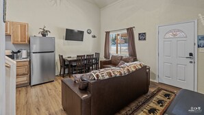 Un espace de vie compact comprenant un coin cuisine, un canapé, une table à manger et une porte agrémentée d’un panneau de verre décoratif.
