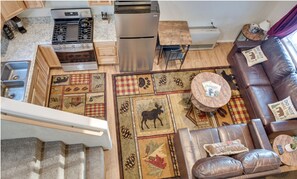 A compact living space with a kitchenette, a brown leather sofa, a round wooden coffee table, and a patterned rug. - Teton Cabin with Loft (Soldotna)