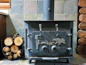 A wood-burning stove with animal carvings, placed next to a stack of firewood.