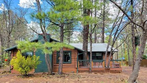 A rustic cabin with a porch and a chimney, surrounded by trees and a clear sky. - The Ohana Lodge - Rustic Log Cabin in Pinetop Country Club w/Deck, BBQ & B-Ball (Pinetop Country Club)