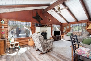 A log cabin interior with a fireplace, wooden furniture, and a ceiling fan.