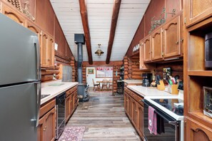 A log cabin interior with wooden cabinets, a central fireplace, and a dining area. - The Ohana Lodge - Rustic Log Cabin in Pinetop Country Club w/Deck, BBQ & B-Ball (Pinetop Country Club)
